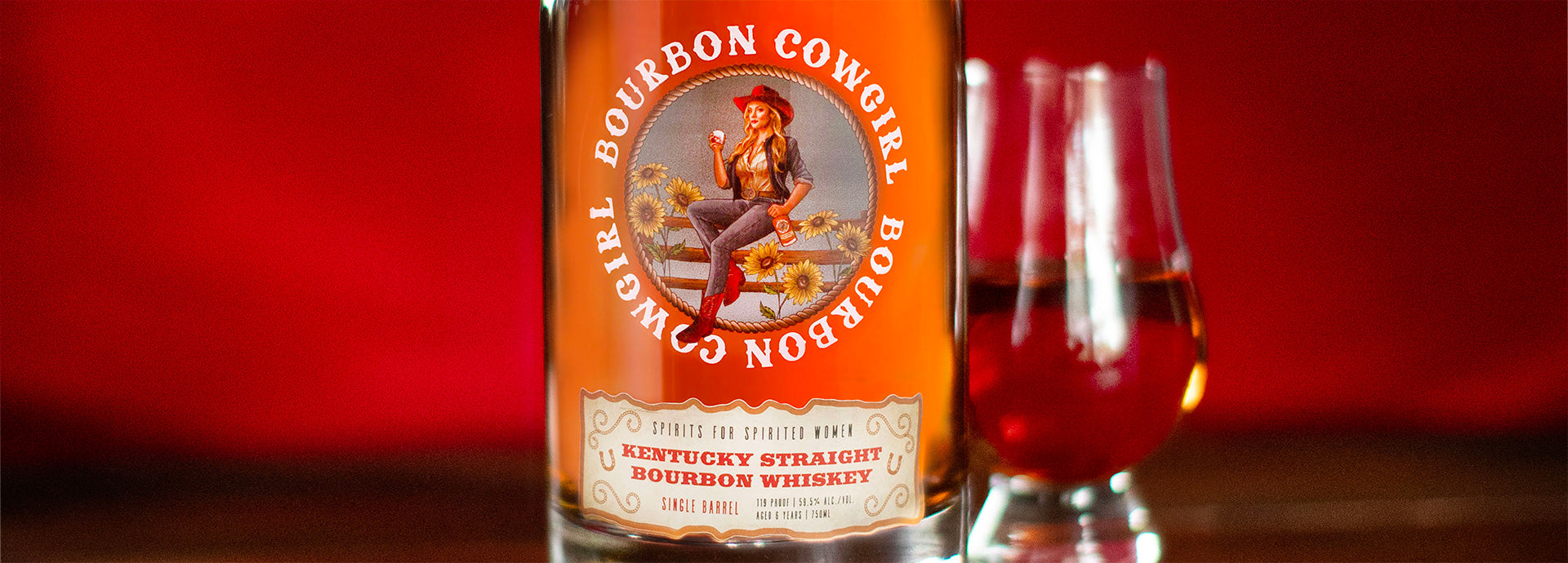 Bottle of Bourbon Cowgirl Single Barrel Kentucky Straight Bourbon Whiskey 750ml on a red background with a whiskey glass